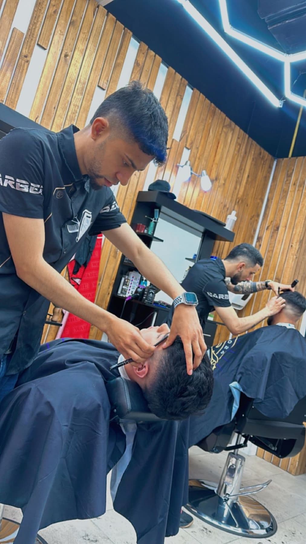 Barbero perfilando la barba de un cliente reclinado en el sillón